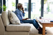 © Wavebreak Media - Smiling african american senior businessman talking mobile phone using laptop on sofa in living room