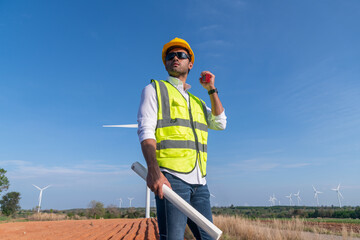 Wall Mural - Engineer wearing uniform ,helmet hold document inspection work in wind turbine farms rotation to generate electricity energy. Green ecological power energy generation wind sustainable energy concept.