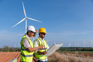 Wall Mural - Engineer wearing uniform ,helmet hold document inspection work in wind turbine farms rotation to generate electricity energy. Green ecological power energy generation wind sustainable energy concept.