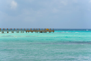 Wall Mural - Seascape. Turquoise sea with clear water and cloudless blue sky. On the horizon is a long pier in the distance.