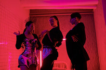 Three Youthful Performers In Posh Apparel Performing Vogue Dance In Modern Night Club While Standing In Front Of Camera