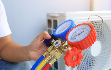 An air conditioner technician's serviceman hand holding a manifold gauge to check the pressure inside the system to normalize the refrigerant charge during high temperatures and hot weather. Maintain.