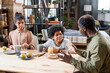 © pressmaster - Contemporary retired black man talking to his grandchildren by table served with peanut butter, bread, apples and tea for breakfast