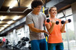 © NDABCREATIVITY - Fit happy woman with her personal fitness trainer in the gym exercising with dumbbells