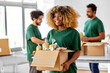 © Syda Productions - charity, donation and volunteering concept - happy smiling female volunteer with food in box and international group of people at distribution or refugee assistance center