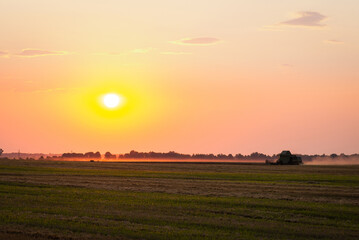 Poster - Combine gathering wheat in the field late in the evening with setting sun in the background