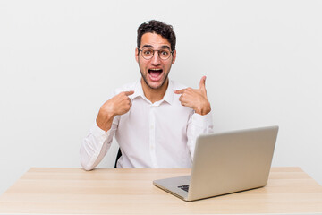 Wall Mural - hispanic handsome man feeling happy and pointing to self with an excited. businessman and desk concept