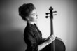 black and white portrait of a cello girl against a light gray wall, a woman holding a cello neck in her hands