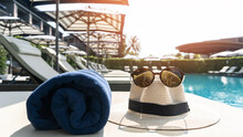 Summer Holiday Vacation Relaxation At Resort Hotel Swimming Pool With Hat And Sunglasses To Protect From UV Sunlight On Sunny Day Sky