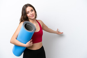 Canvas Print - Young sport caucasian woman going to yoga classes while holding a mat isolated on white background extending hands to the side for inviting to come