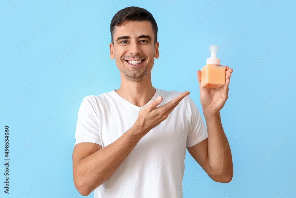 Handsome young man with liquid soap on blue background