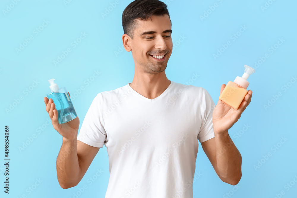Handsome young man with different liquid soap on blue background