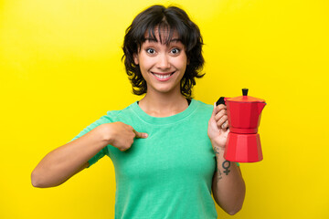 Wall Mural - Young Argentinian woman holding coffee pot isolated on yellow background with surprise facial expression