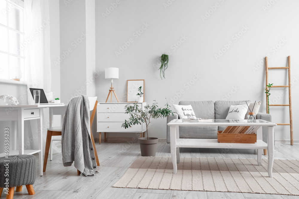 Interior of light living room with coffee table, sofa and workplace