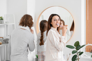 Wall Mural - Young woman with her husband and little daughter brushing teeth in bathroom