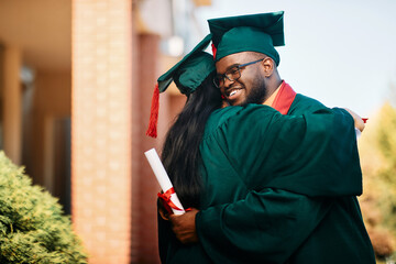 Wall Mural - Happy black college student and his female friend hug each other while celebrating their graduation.