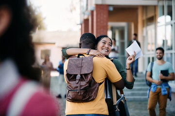 Wall Mural - Happy Asian student hugs her African American boyfriend after passing an exam at the university.