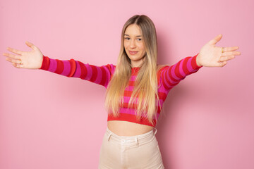 Wall Mural - Young cheerful girl happy positive isolated on pink background feels confident giving a hug to the camera.