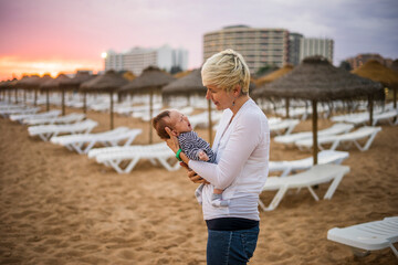 Wall Mural - Mother with her newborn baby boy bonding at the beach in the resort by sunset