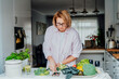 Middle age woman checking cooking tutorial video on her phone while preparing broccoli dish in a kitchen. Online recipes. Mobile app with diet program. Healthy lifestyle, weight loss concept
