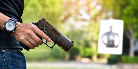 Automatic black 9mm pistol gun holding in hands of shooter and ready to aim to the man-target shooting paper ahead, concept for training and practising human to be body guard and vip protectors.