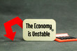 calculator, down arrow and wooden tag with the words the economy is unstable