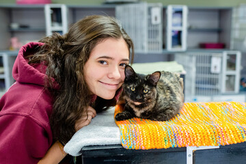 brunette teen smiles at camera with a cat at a shelter