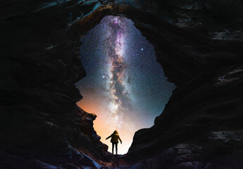 Wall Mural - silhouette of a person in the cave looks on the bright milky way galaxy. fantasy scene.
