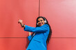 © Dani D.G - Urban dancer of African ethnicity, dancing and laughing while listening to music with her smartphone outdoors. Woman in blue clothes on red background, celebrating and enjoying her feeling of freedom.
