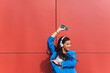 © Dani D.G - African ethnicity student happy and smiling while dancing and listening to music with energy and joy, celebrating weekend, vacation or school grades. Blue clothes and red color background wall.