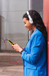 © Dani D.G - Smiling African girl using her mobile phone outdoors.Vertical shot of a 20 year old girl listening to music leaning against a red wall.