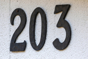 Closeup of house number 203 on white concrete wall