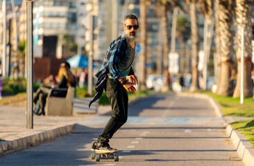 Canvas Print - latin senior man with beard skateboard on bikeway in La Serena