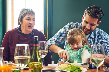 Poster - Let me help you there dear. Shot of a cheerful young man helping to cut his daughters food while being seated around a dinner table at home.