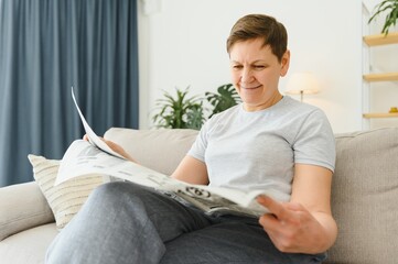 Canvas Print - middle aged woman sitting sofa and reading newspapers.