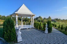 Octagon Gazebo With Small Trees Adorning It In And Paved Walkway.