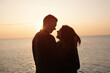 © eduard - Silhouette of young happy smiling couple hugging over sunset background on the sea beach.