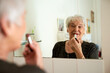 © Tamani Chithambo/peopleimages.com - Youre never too old to play the femme fatale. Portrait of a happy senior woman applying makeup while looking in the mirror.