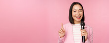 Image Of Enthusiastic Asian Businesswoman Giving Speech, Talking With Microphone, Holding Mic, Standing In Suit Against Pink Studio Background