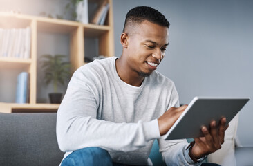 Poster - Just having a quick browse online. Shot of a handsome young man using his digital tablet while sitting on a sofa at home.