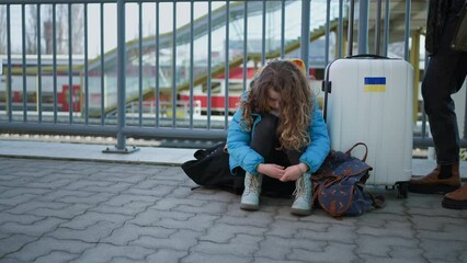 Wall Mural - Sad Ukrainian immigrant child with luggage waiting at train station, Ukrainian war concept.