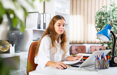 Wall Mural - Young clerical worker sitting at desk in office and using laptop for work.