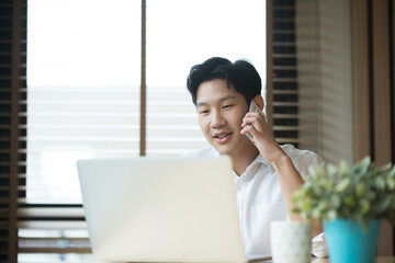 Asian man working while making phone call and using laptop at home