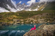 Hiking woman in red jacket sitting at beautiful lake in mountains.