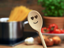 wooden cooking spoon with heart smiley in front of saucepan with spaghetti and other ingredients for a perfect pasta sauce, cooking with love at home for a good relationship or a happy family