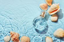 Glass Perfume Bottle And Sea Shells In Spray Water Background. Marine Summer Fragrance Concept