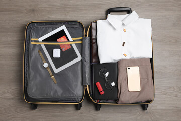 Poster - Folded clothes and accessories in open suitcase on wooden background, top view. Packing for business trip