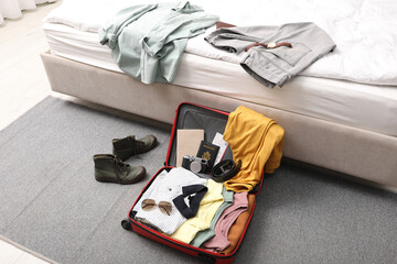 Poster - Open suitcase with clothes, accessories and shoes on floor near bed indoors