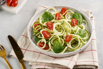 Keto paleo low-carb zoodles: zucchini noodles with parmesan cheese, cherry tomatoes, quil eggs on light grey surface