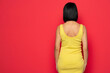 Rear view of a standing  woman in yellow tight dress over isolated red background